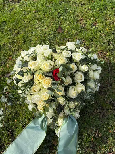 Herzförmiges Trauergesteck aus weißen Rosen mit roter Rose